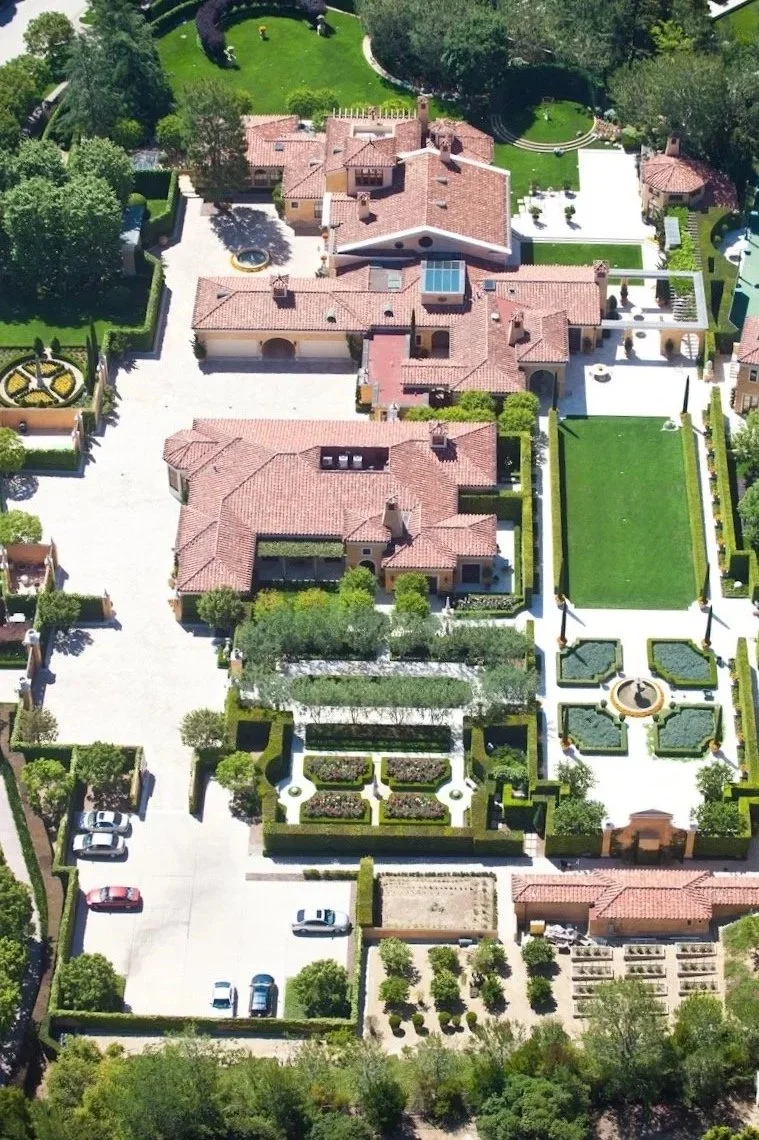 An aerial view of a large, luxurious estate with multiple buildings, well-manicured gardens, and a spacious parking area.
