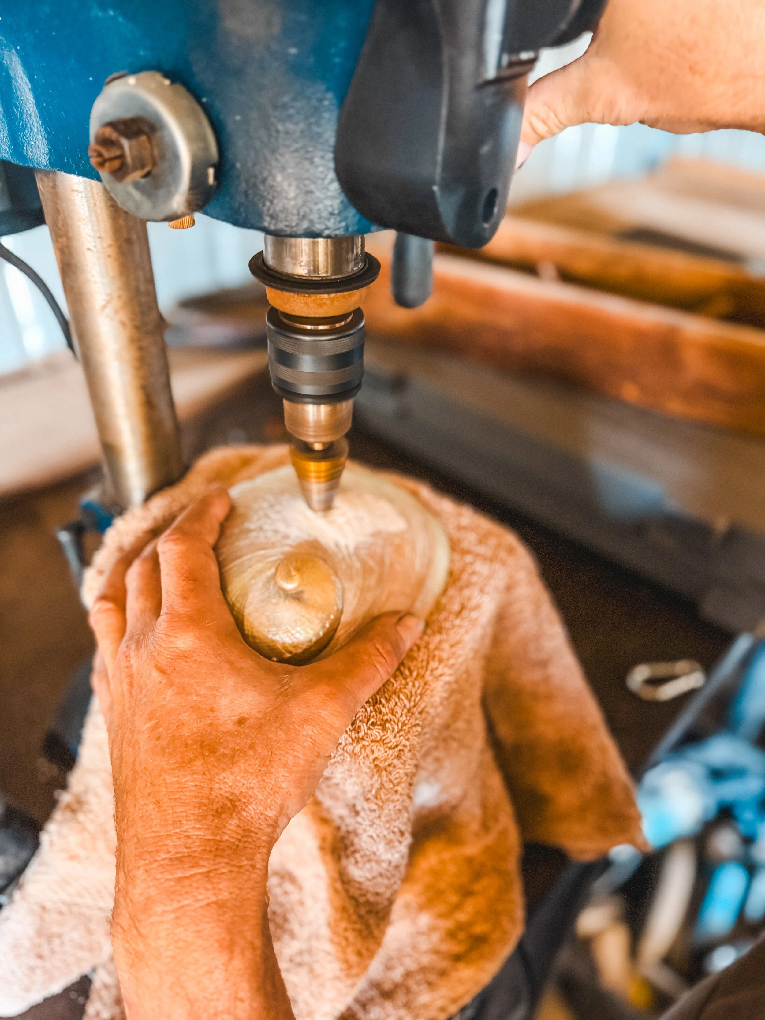 A person is using a drill press to carve or work on abalone shell.
