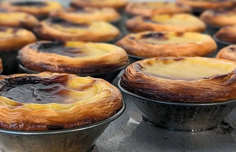 Close-up of multiple egg tarts in black ceramic bowls on a baking sheet.