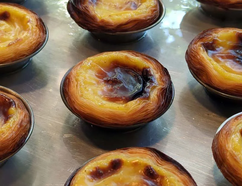 Multiple pastel de nata, Portuguese egg custard tarts, on a reflective surface.