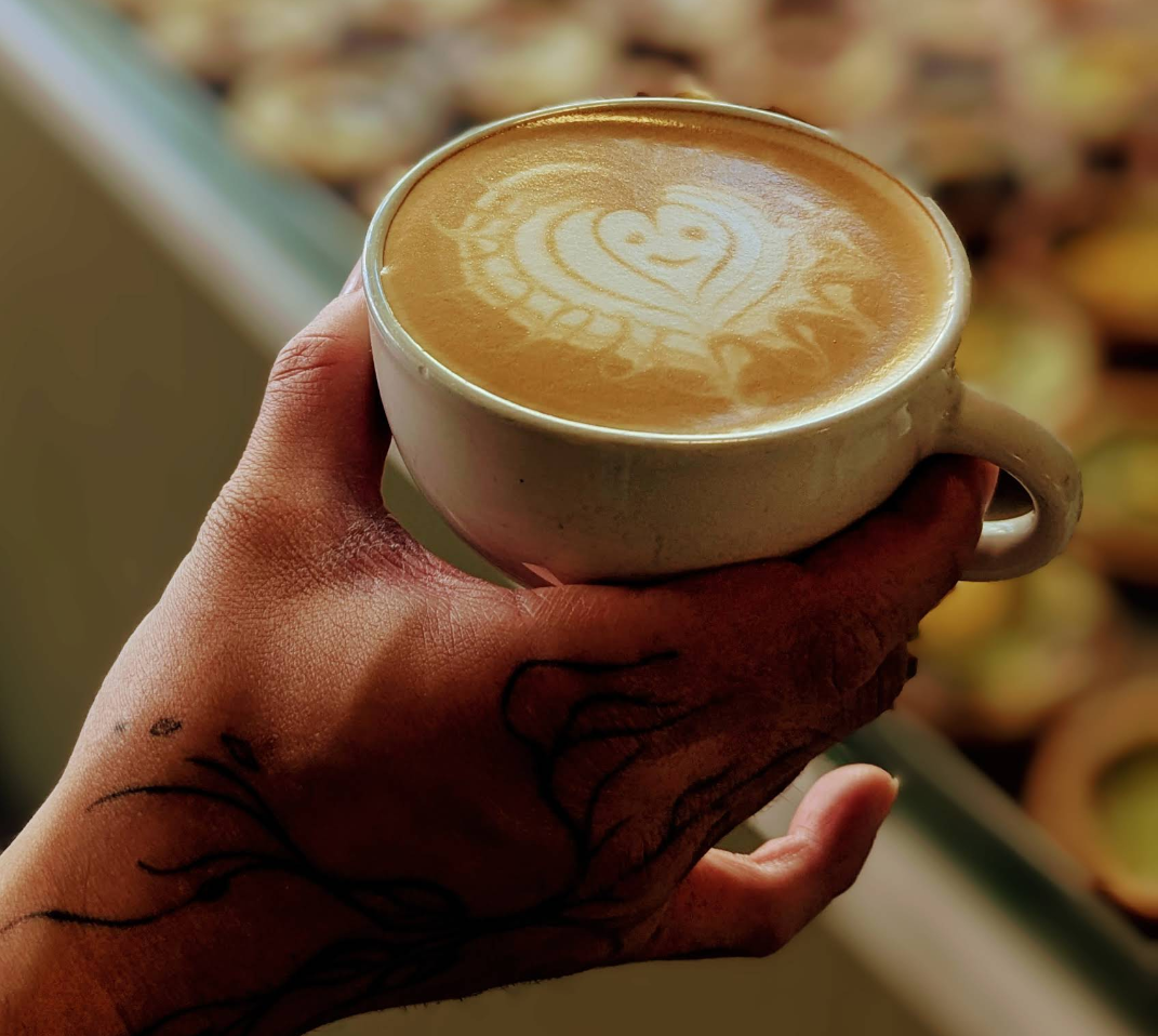 A person holding a white mug with a latte art heart design on the foam.
