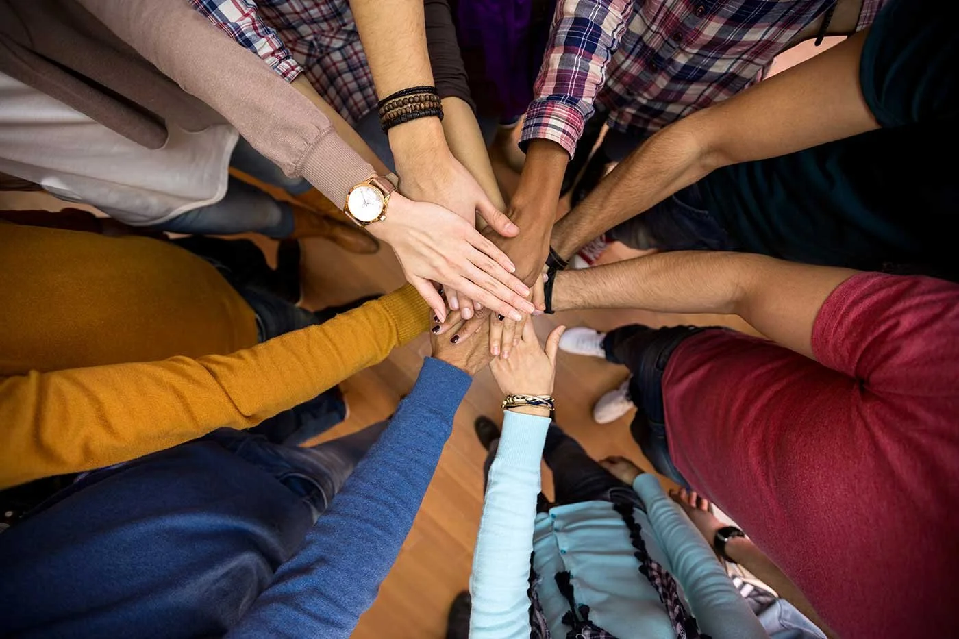 A group of diverse people placing their hands on top of each other in a gesture of teamwork and unity.