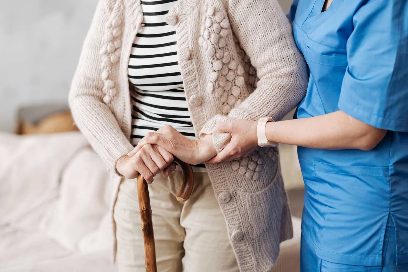 A caregiver helping an elderly woman walk with a cane, supporting her arm as she receives assistance in a home setting.