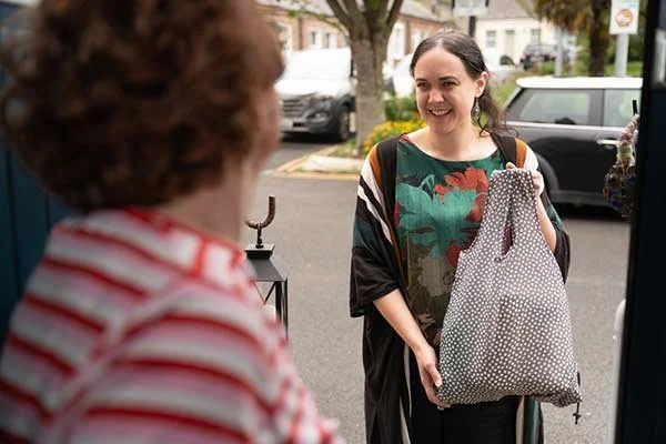 A young woman smiling as she receives a large polka-dotted bag from an older woman on a sidewalk.