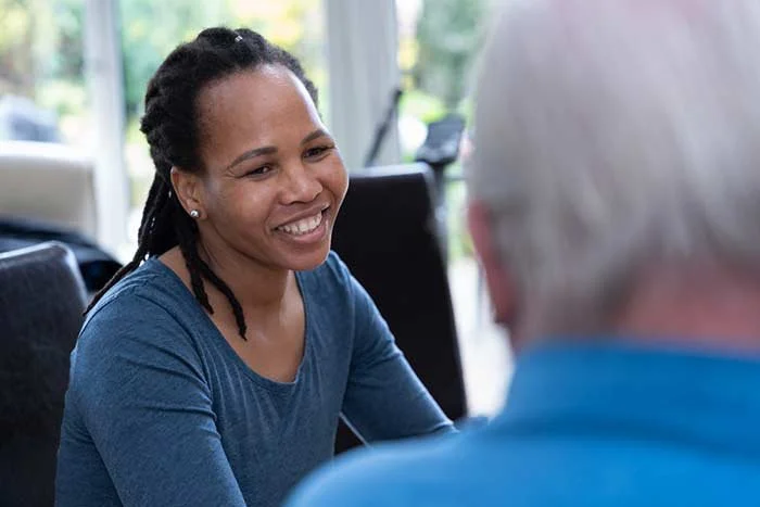 A woman smiling while talking to an older man in a bright, indoor setting.