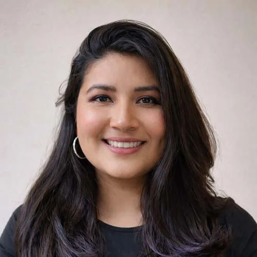 A smiling woman with long dark hair and hoop earrings, wearing a black shirt, against a plain background.