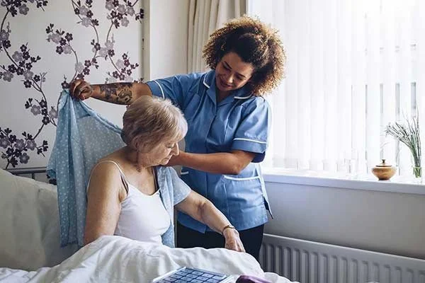A caregiver helping an elderly woman in bed in a well-lit room.