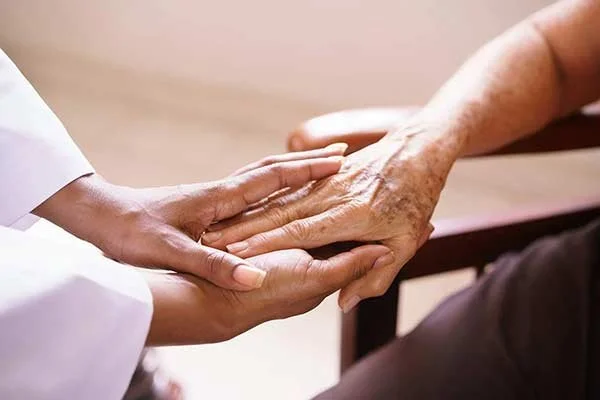 A healthcare worker holding an elderly person's hand in a comforting gesture.