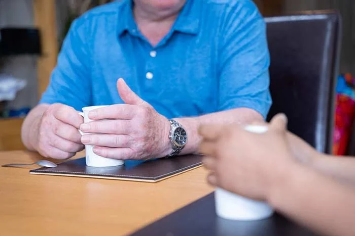 A person in a blue shirt holding a white mug with both hands at a table.