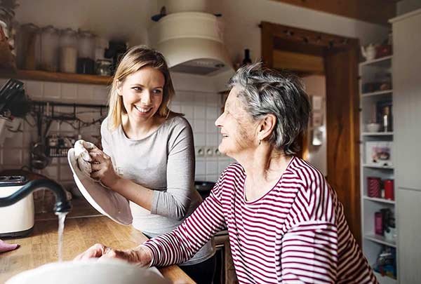 A young woman and an elderly woman smiling and doing dishes together in a kitchen.
