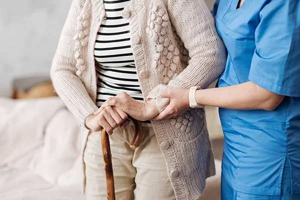 A healthcare worker helping an elderly woman with her walk, holding her arm for support.