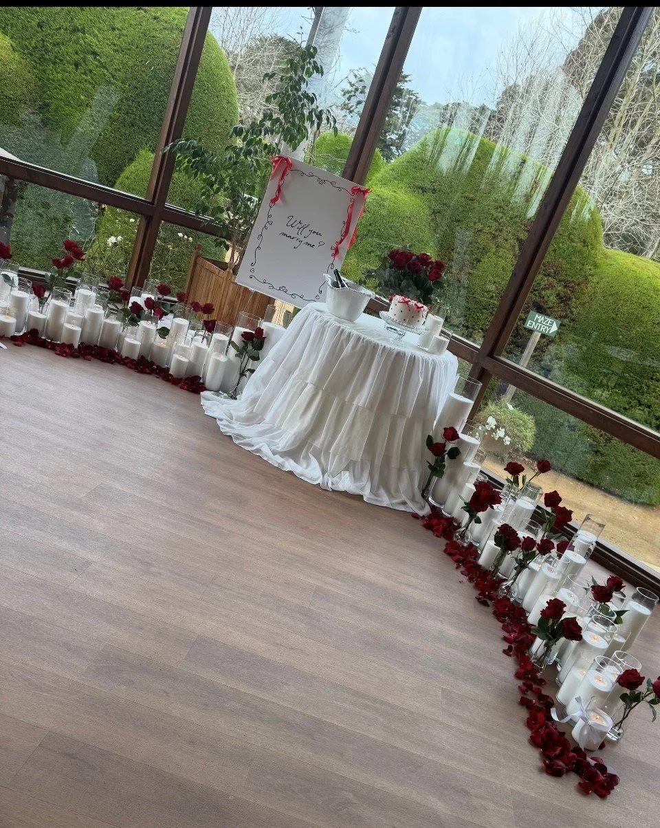 Elevated proposal setup featuring a styled table with soft fabrics, candlelight, roses, and custom signage in an indoor Melbourne location
