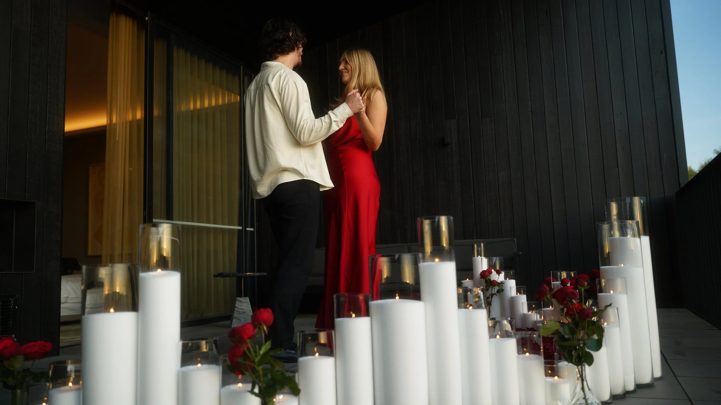 Candle-focused intimate proposal setup with pillar candles, roses, and a couple sharing a romantic proposal moment in an indoor Melbourne location