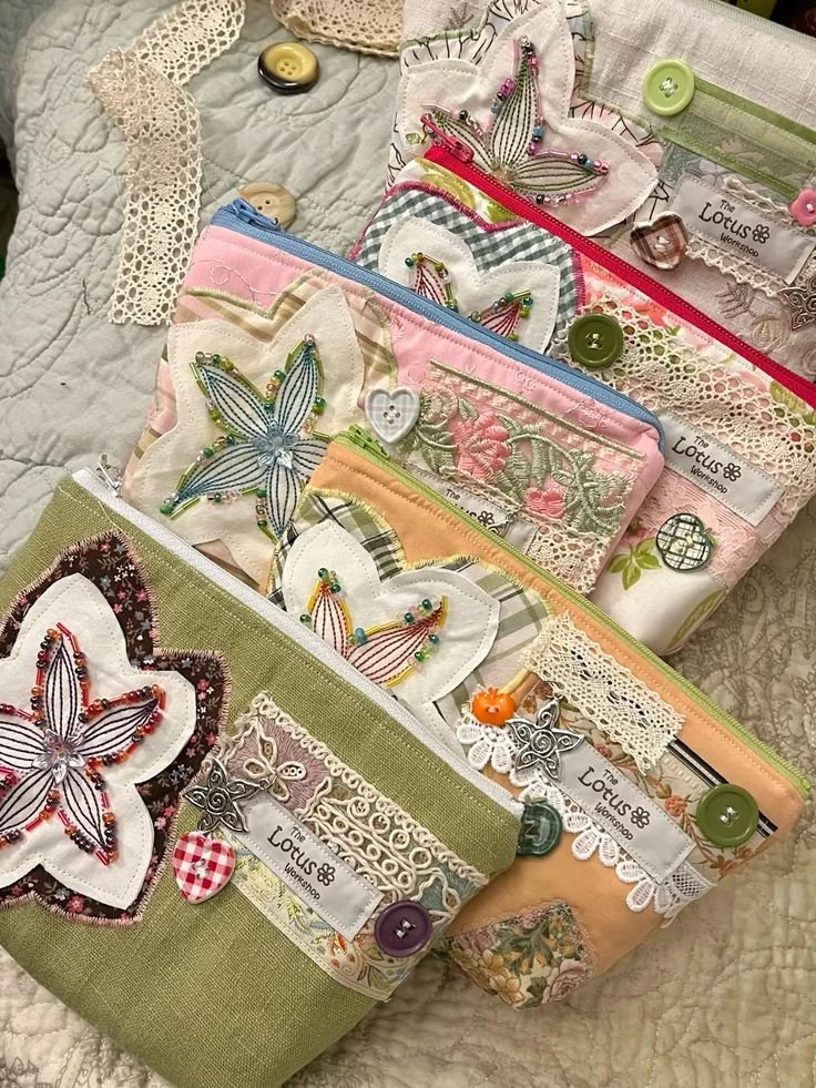 Multiple embroidered pouches with floral and butterfly designs, decorated with lace, buttons, and charms, laid out on a quilted fabric.