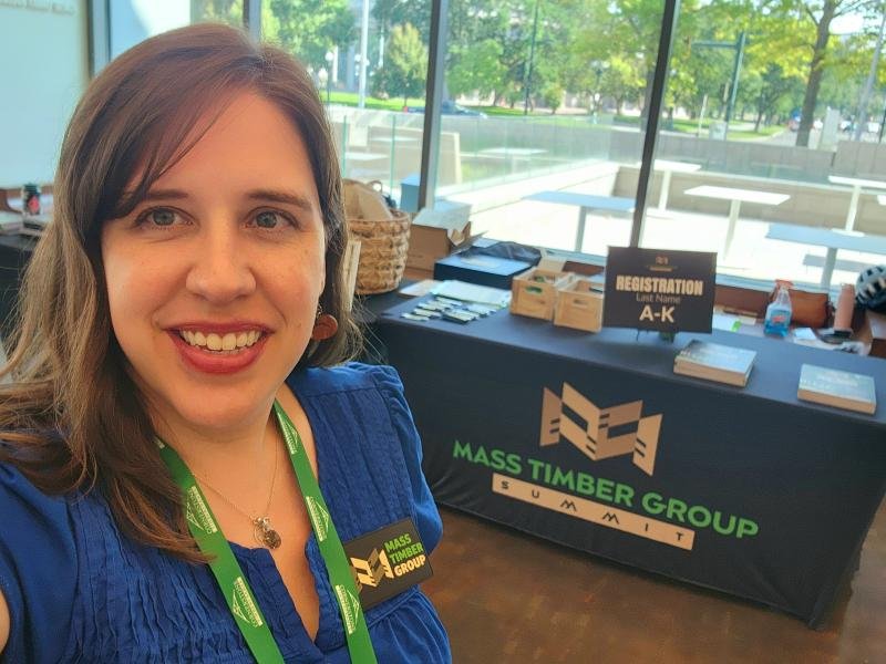 Photo of Candra near a registration table at the mass timber group summit in Denver, Colorado.