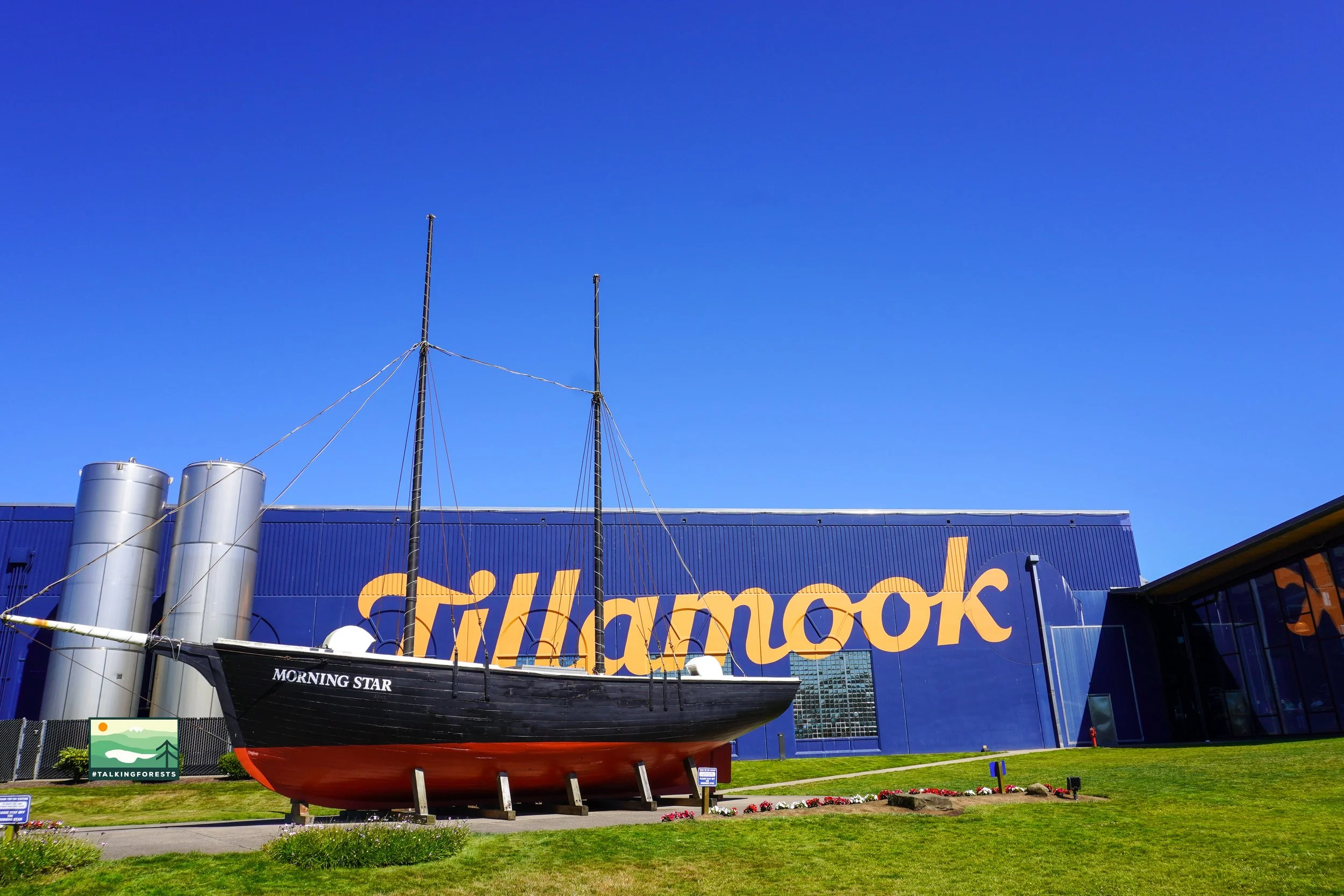 A blue building with Tillamook written all over the side of it. Morning Star, the boat that has a story behind it from the Tillamook area and green grass.