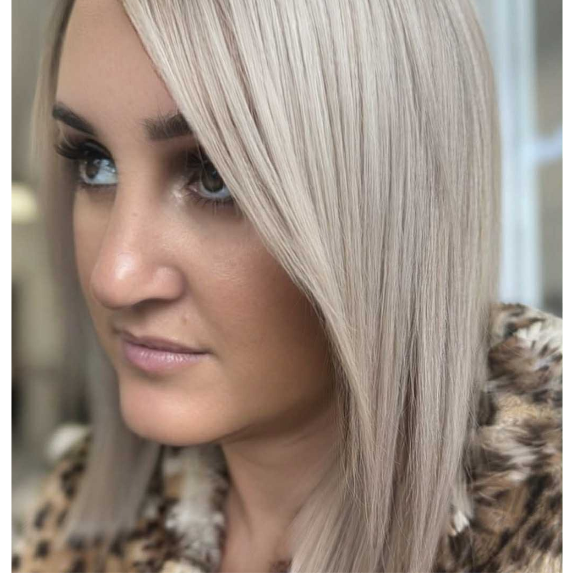 Close-up of a woman with platinum blonde, straight hair and makeup, wearing a leopard print coat.