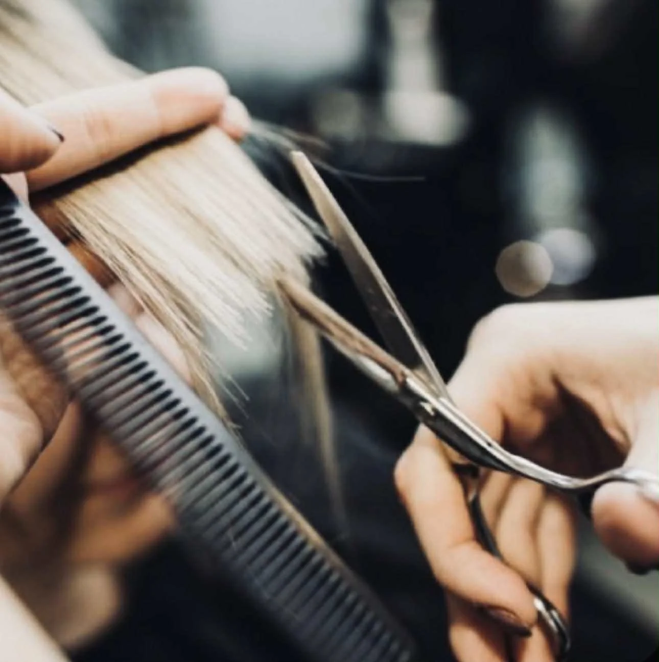 Close-up of a hairstylist cutting blonde hair with scissors, with a comb holding the hair in place.