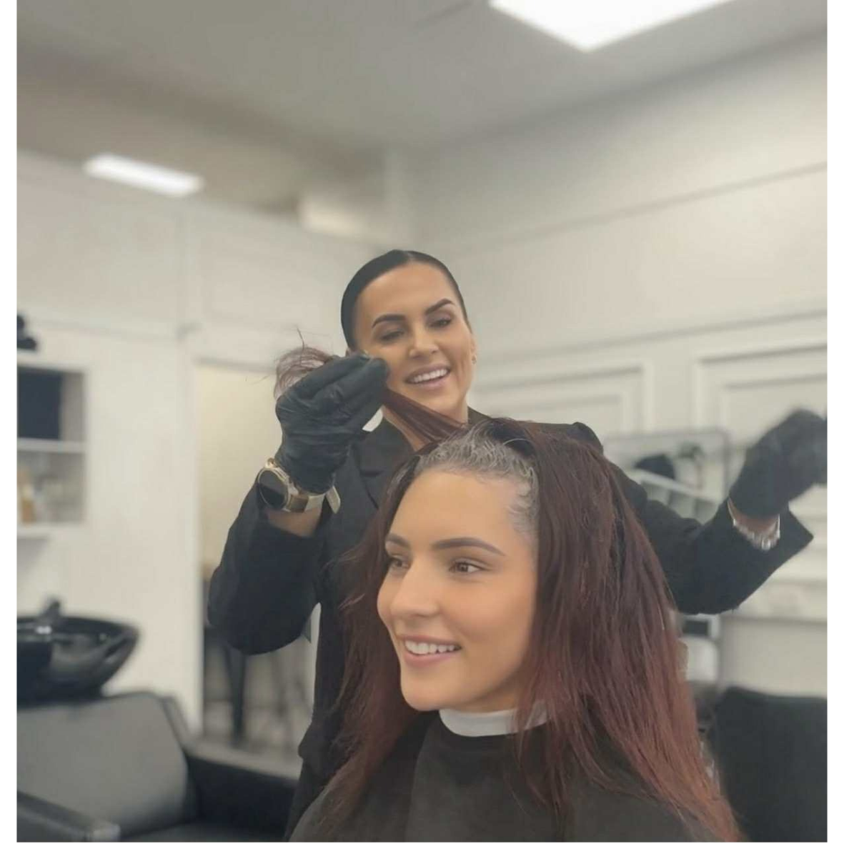 A woman getting her hair colored by a hairstylist in a salon. The hairstylist is smiling while working on the woman's hair.