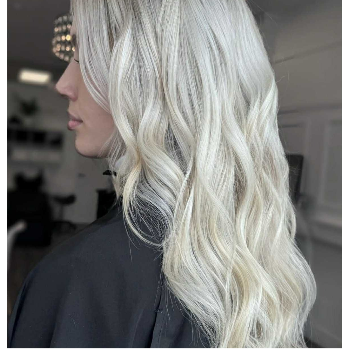 Woman with long, wavy platinum blonde hair styled in loose curls, shown from side profile.