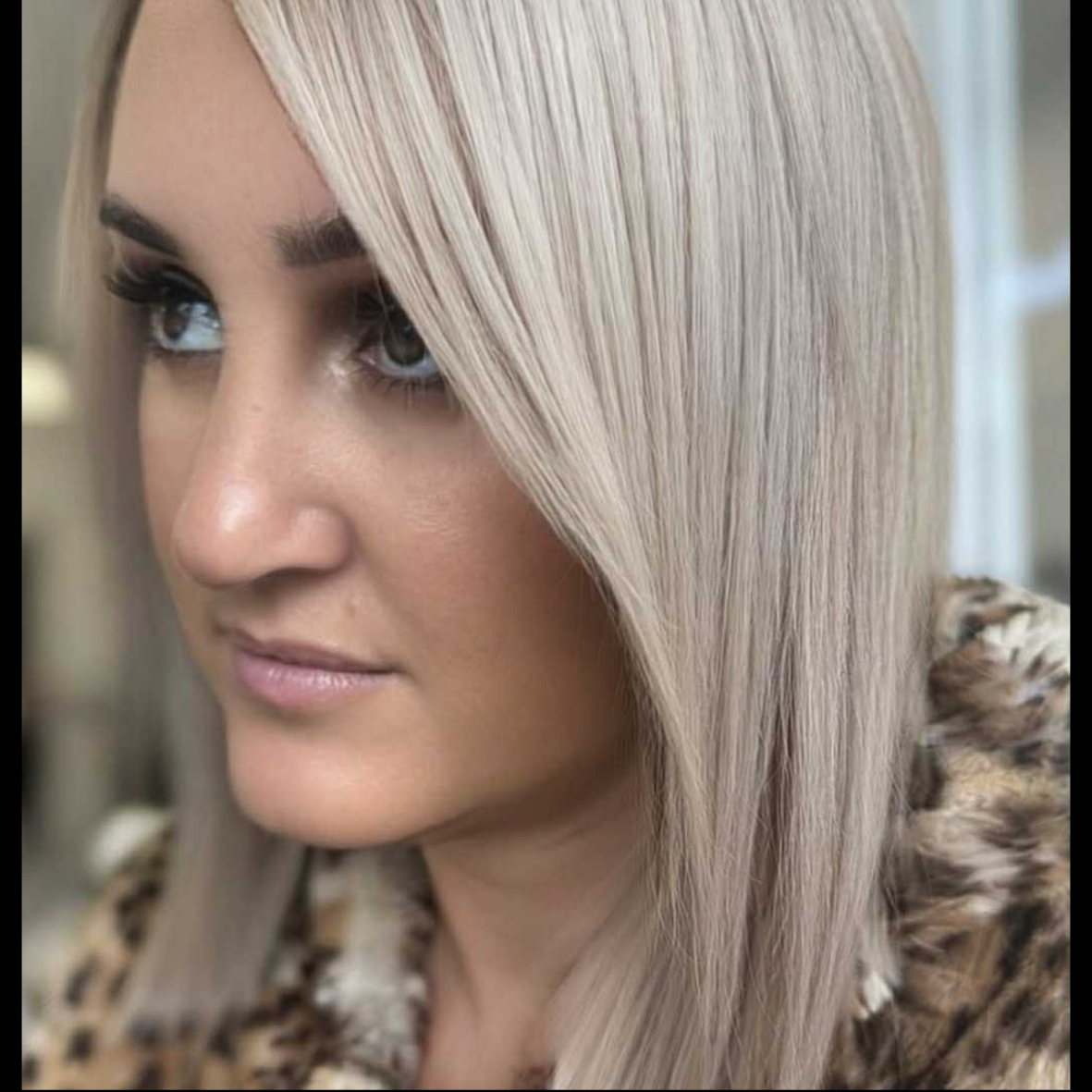 Close-up of a woman with platinum blonde hair and gray eyes, wearing a leopard-print top.