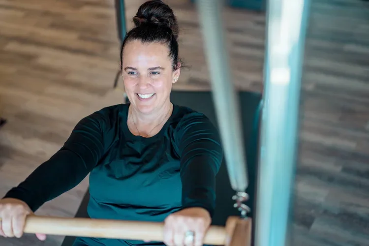 Woman with dark hair in a bun exercising on a Pilates machine in a gym.