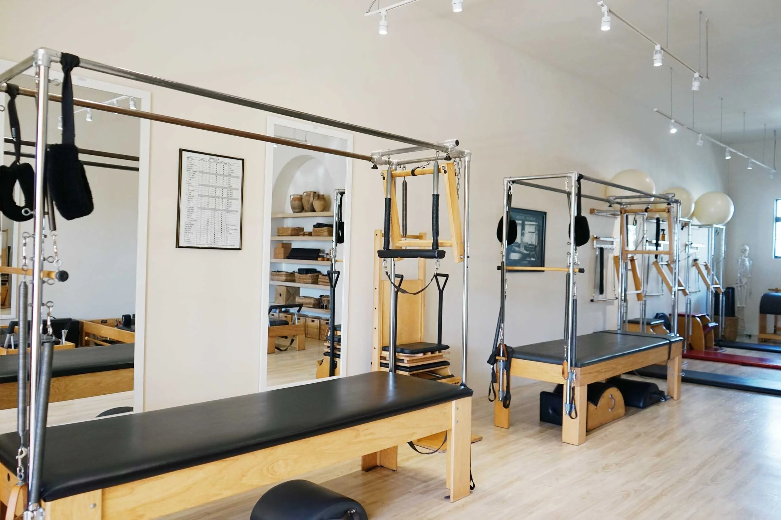 Pilates or physical therapy studio with wooden equipment and mats, large windows, and bright lighting.