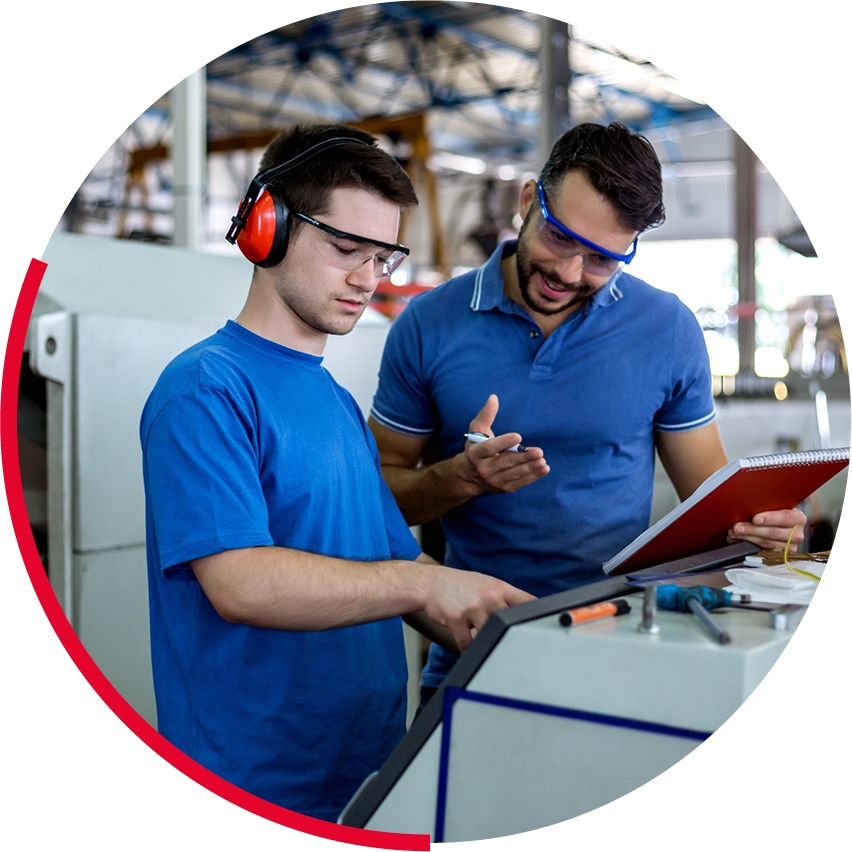 Deux hommes en bleu travaillent avec des machines dans un atelier, portant des lunettes de protection.