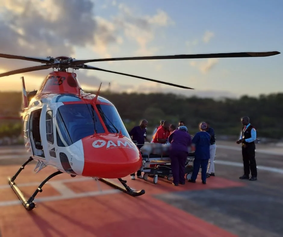 Medical team attending to a patient on a stretcher next to a rescue helicopter on a helipad during sunrise or sunset.