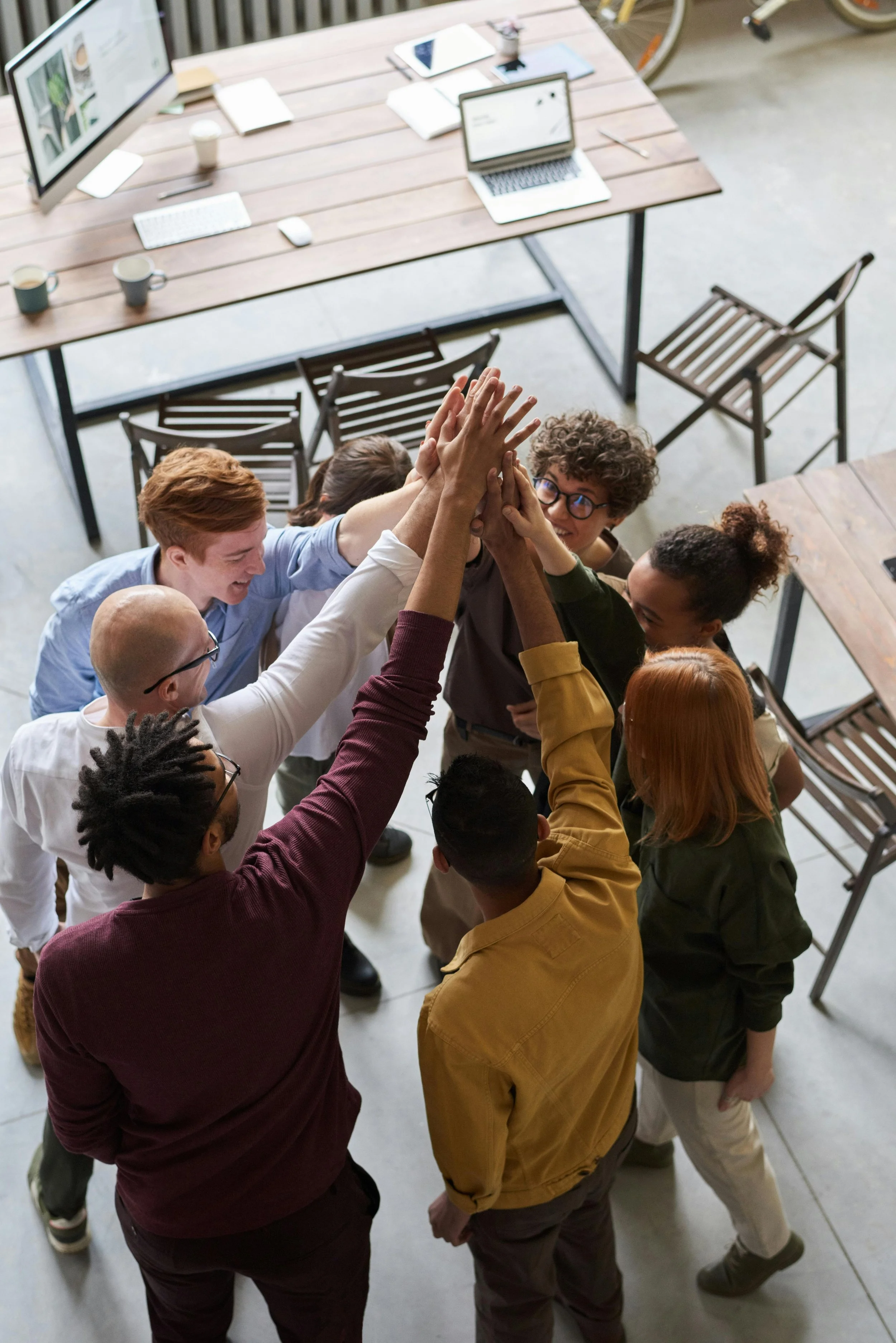 Group of diverse coworkers high-fiving each other in an office with a desk and computers in the background.