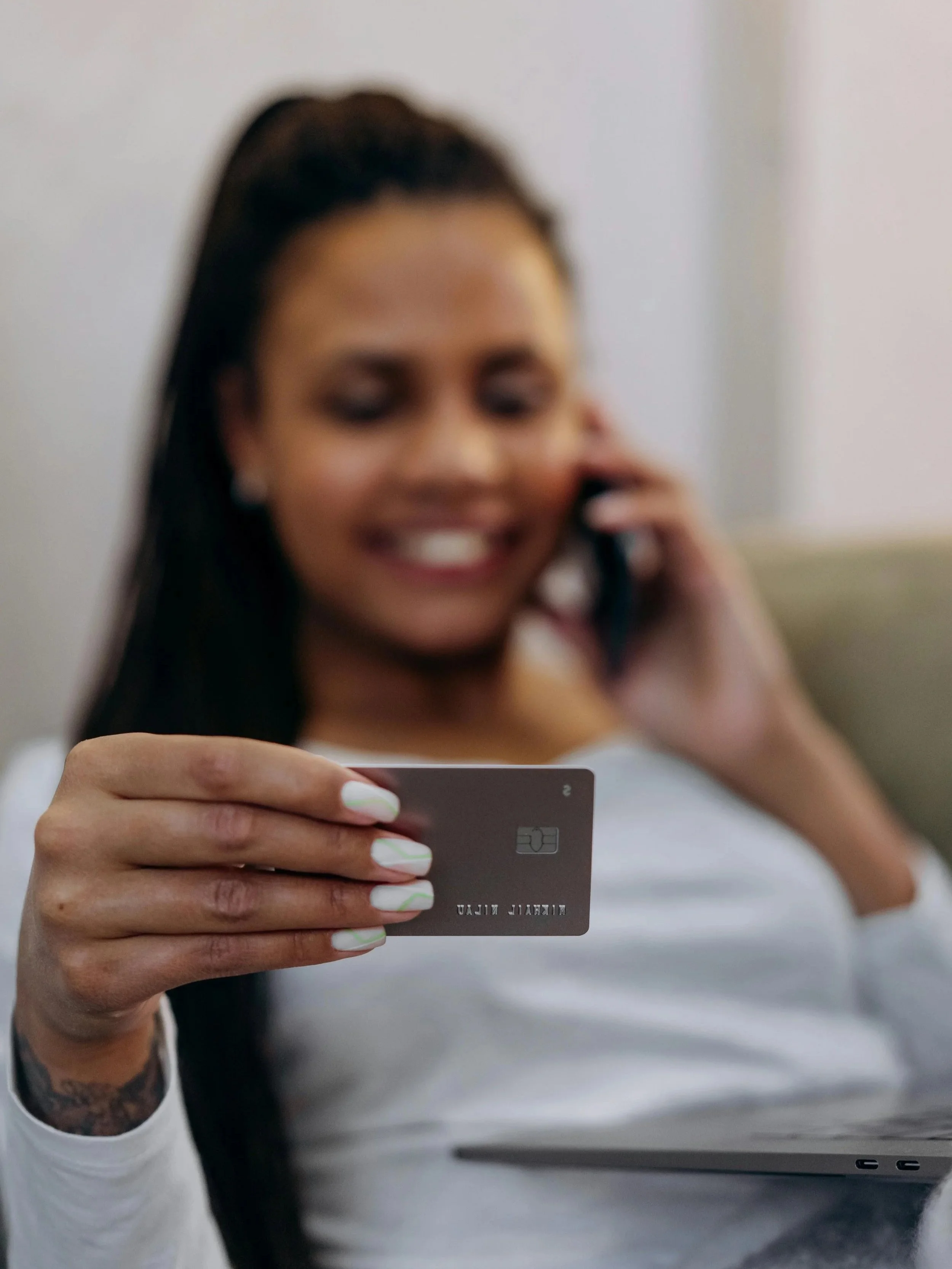 A woman with long dark hair, smiling and talking on the phone, holding a credit card in her hand.