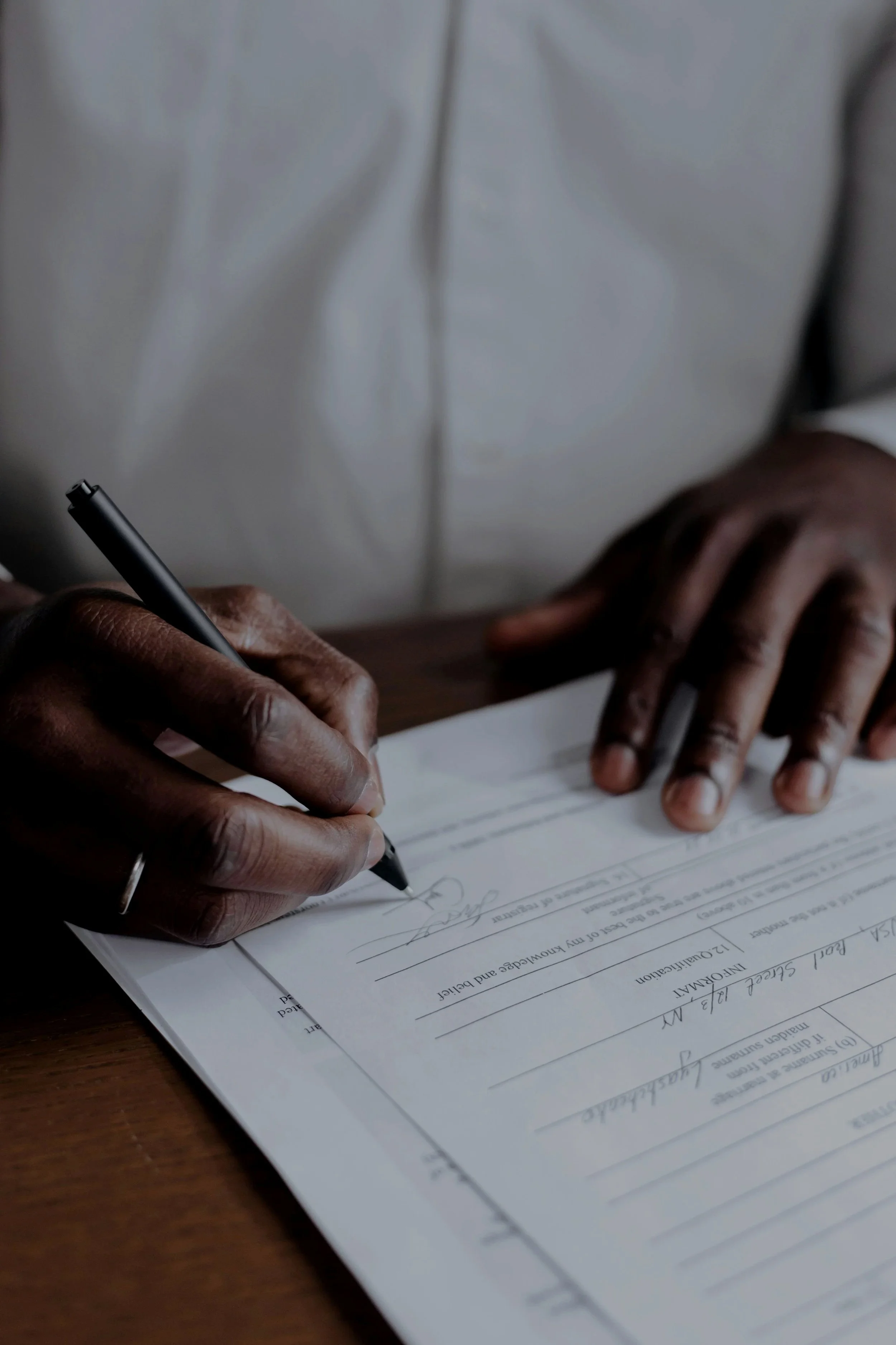 A person signing a document with a black pen at a wooden table.