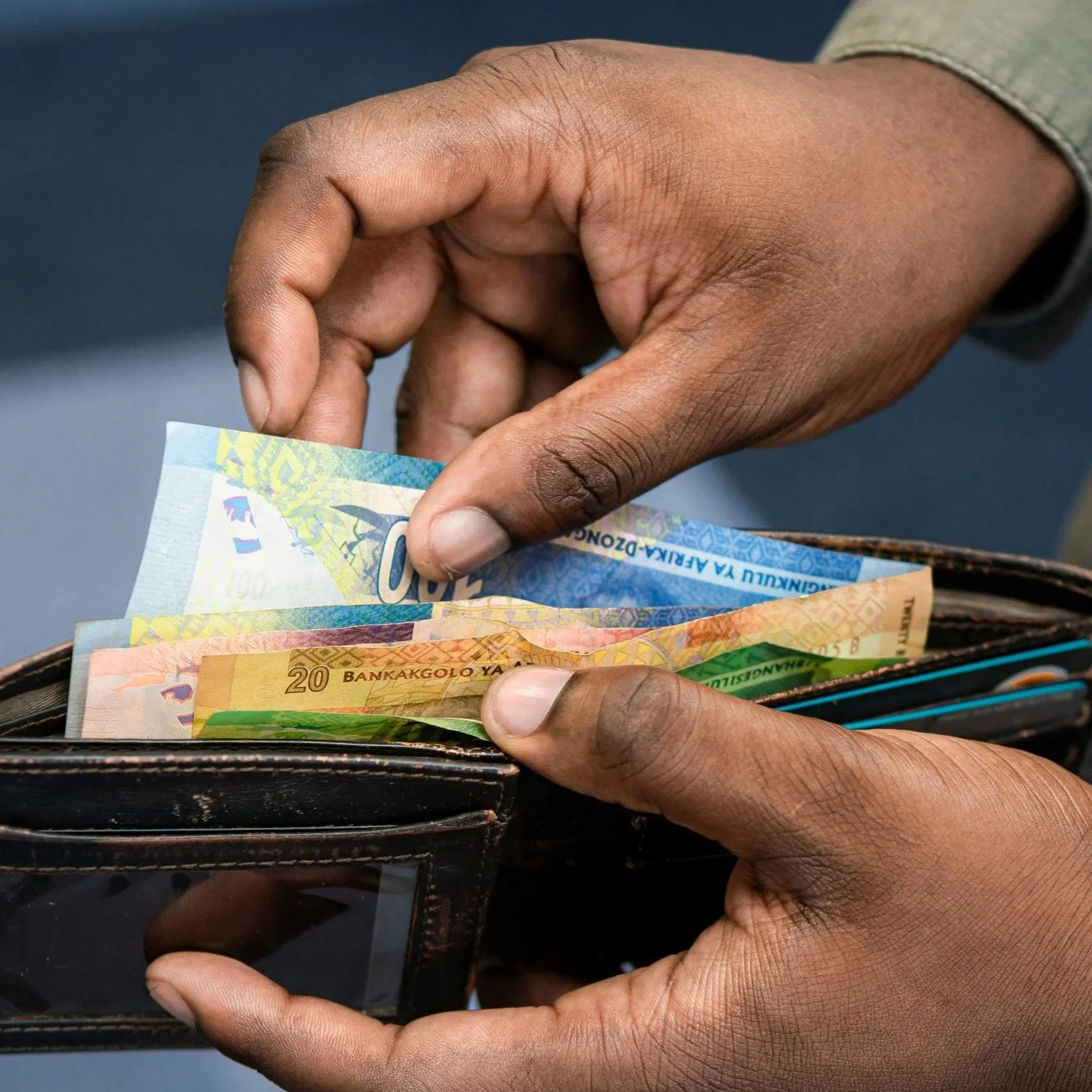 Person's hands holding a wallet with banknotes in various colors and denominations.
