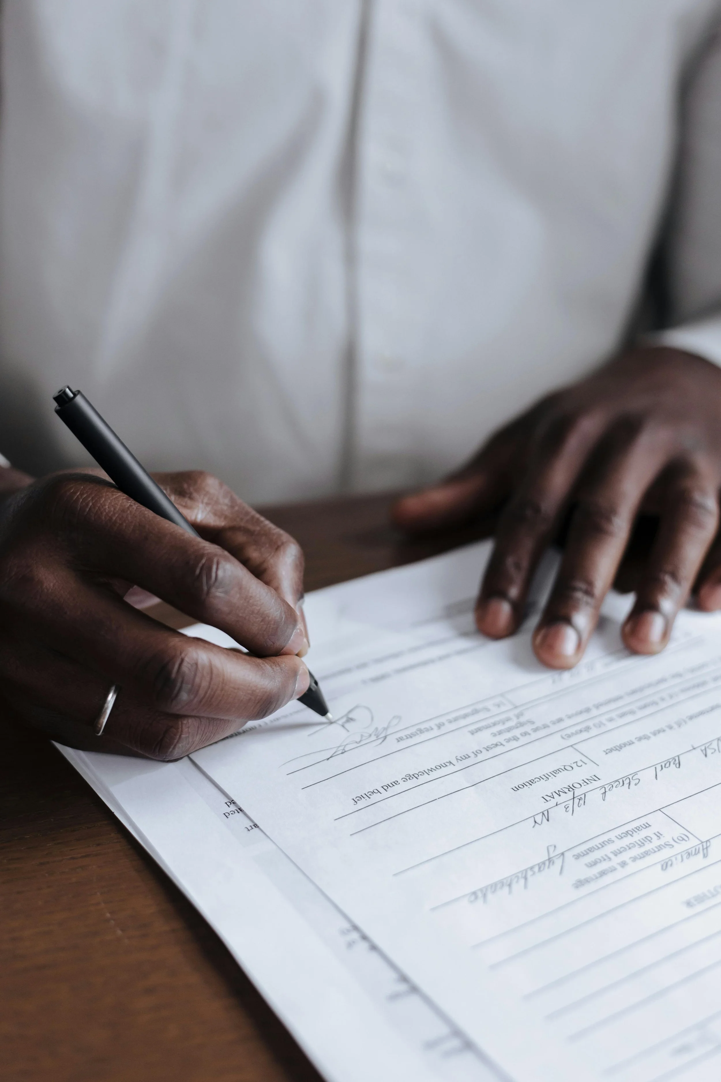 A person signing a document on a wooden desk with a black pen.