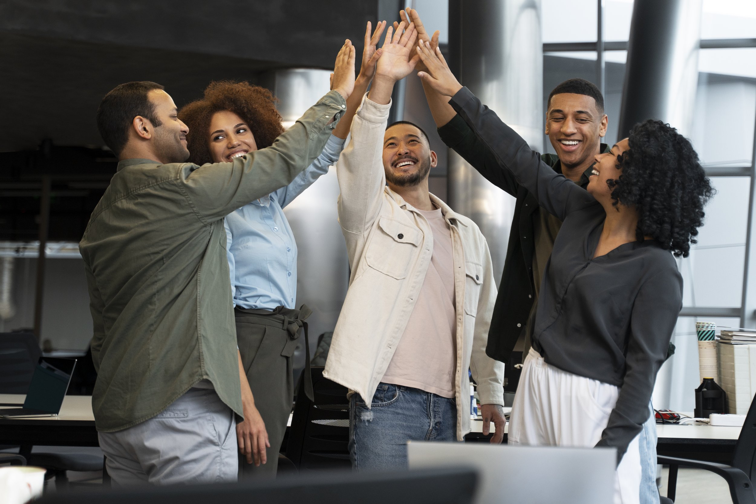 Six diverse coworkers in a modern office giving each other high fives and smiling.