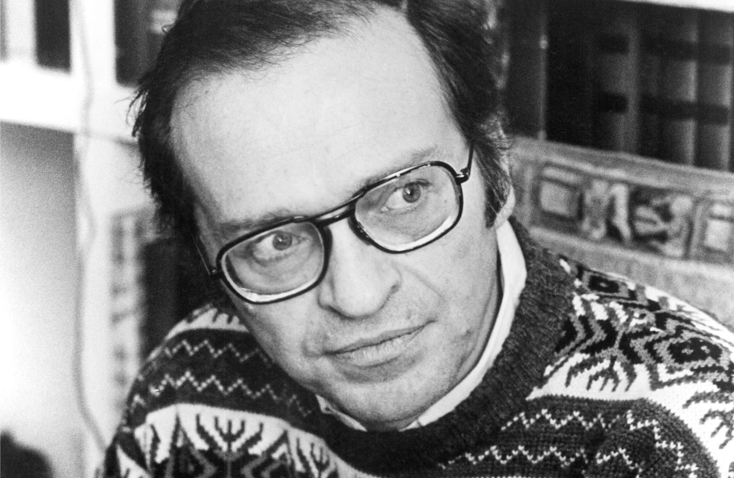 Black and white photograph of a Sidney Lumet man wearing glasses, a patterned sweater, and a collared shirt. He is looking to his left with a slight smile.