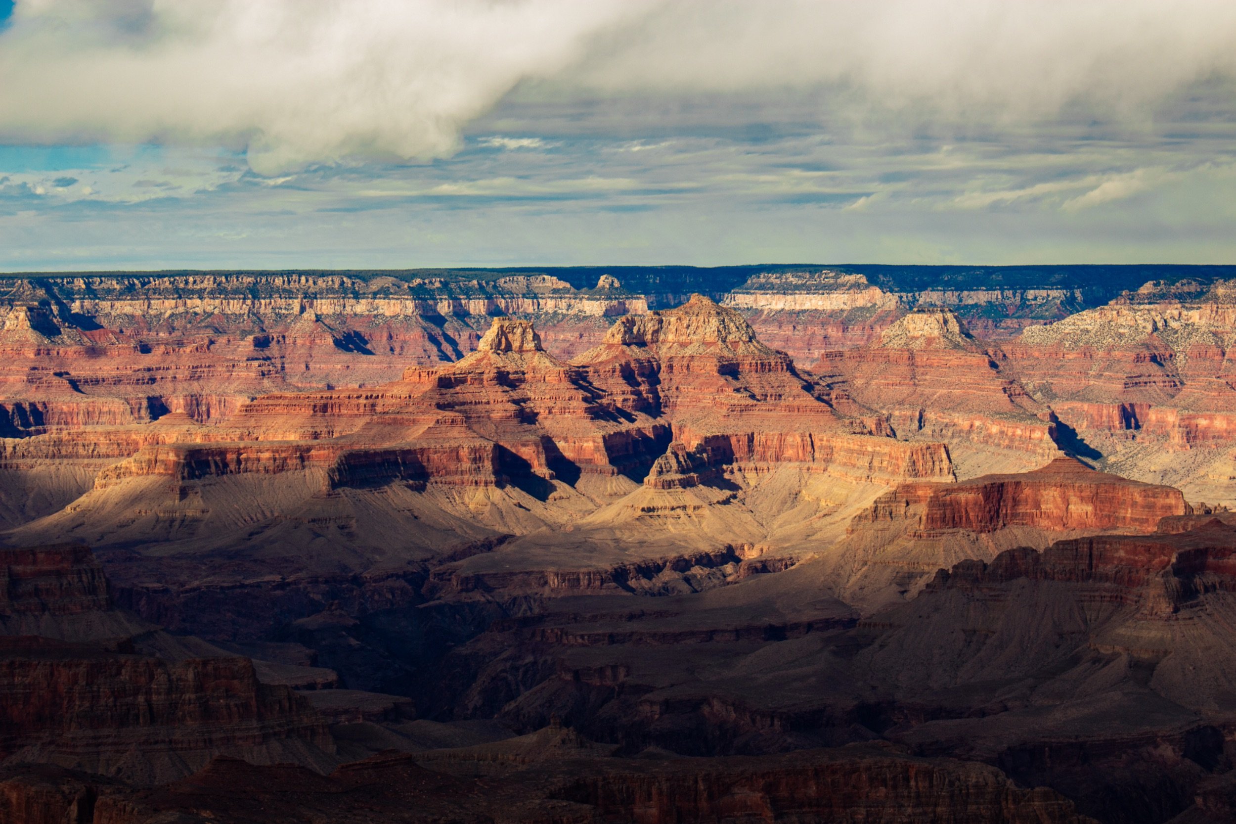 View of the Grand Canyon with layered rock formations and a cloudy sky.