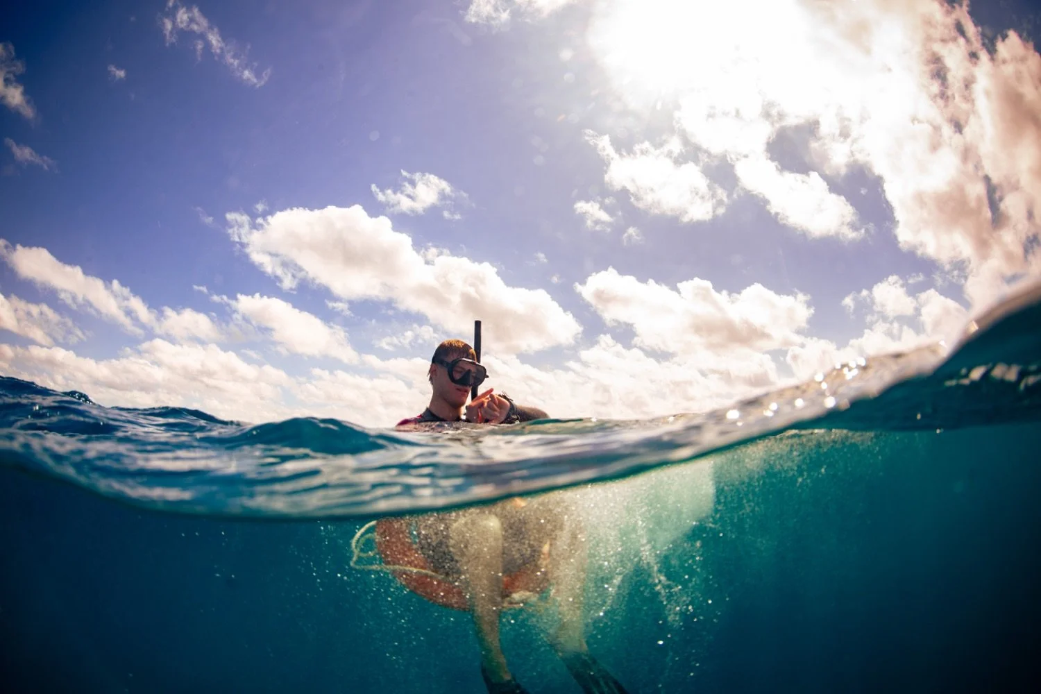 A person in snorkeling gear floating in the ocean, with the sky and clouds visible above the water.