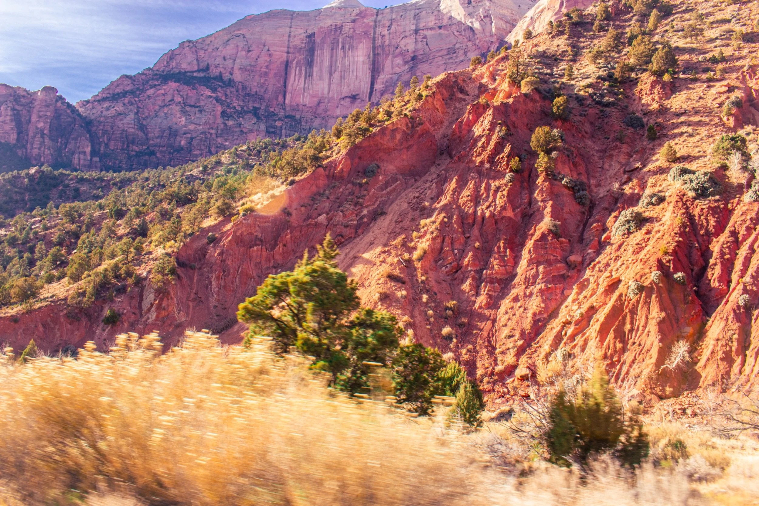 Colorful rocky canyon landscape with reddish and purple cliffs and sparse greenery.