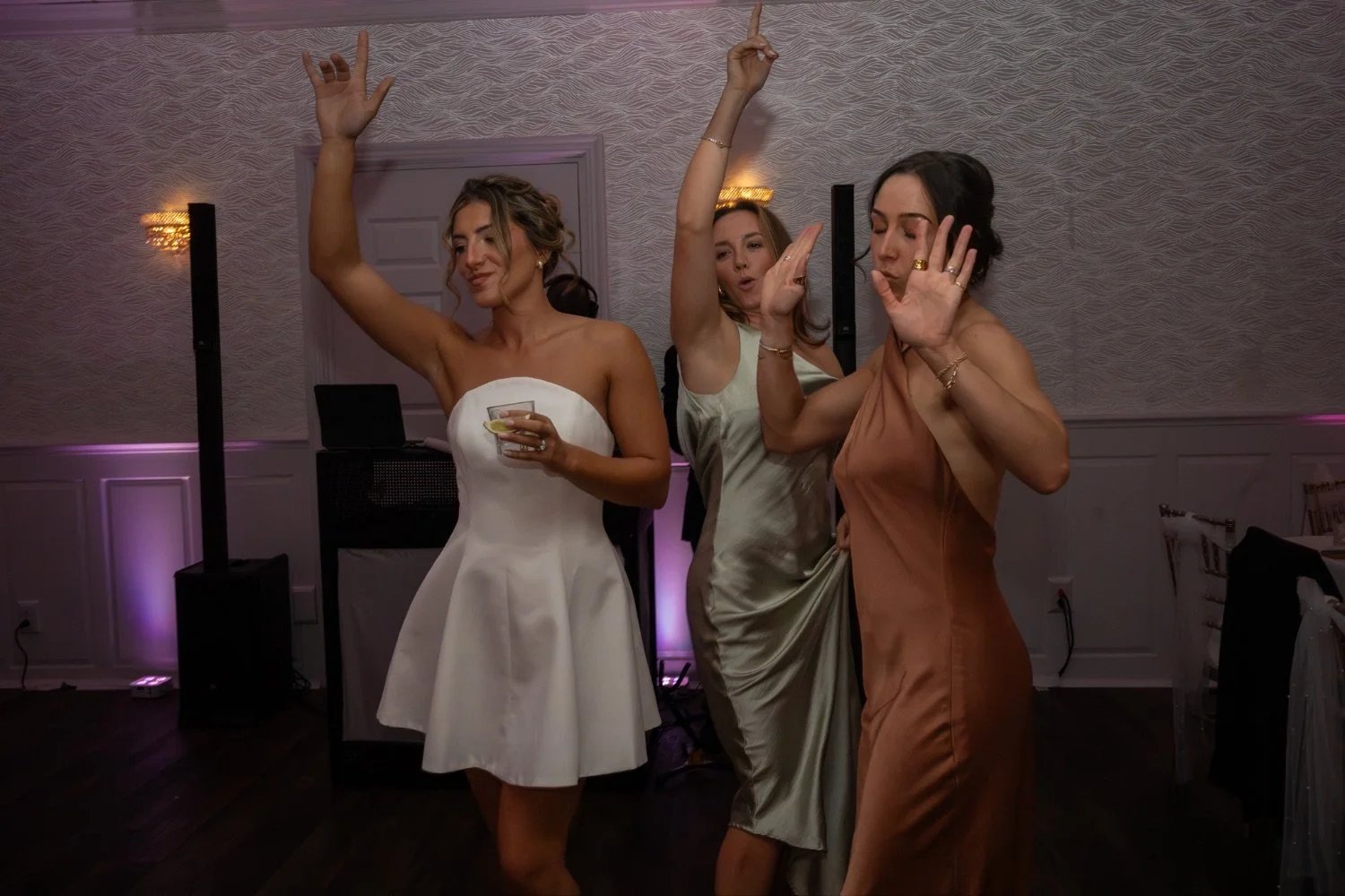 Three women dancing at a party or celebration, one holding a drink with a lemon slice.