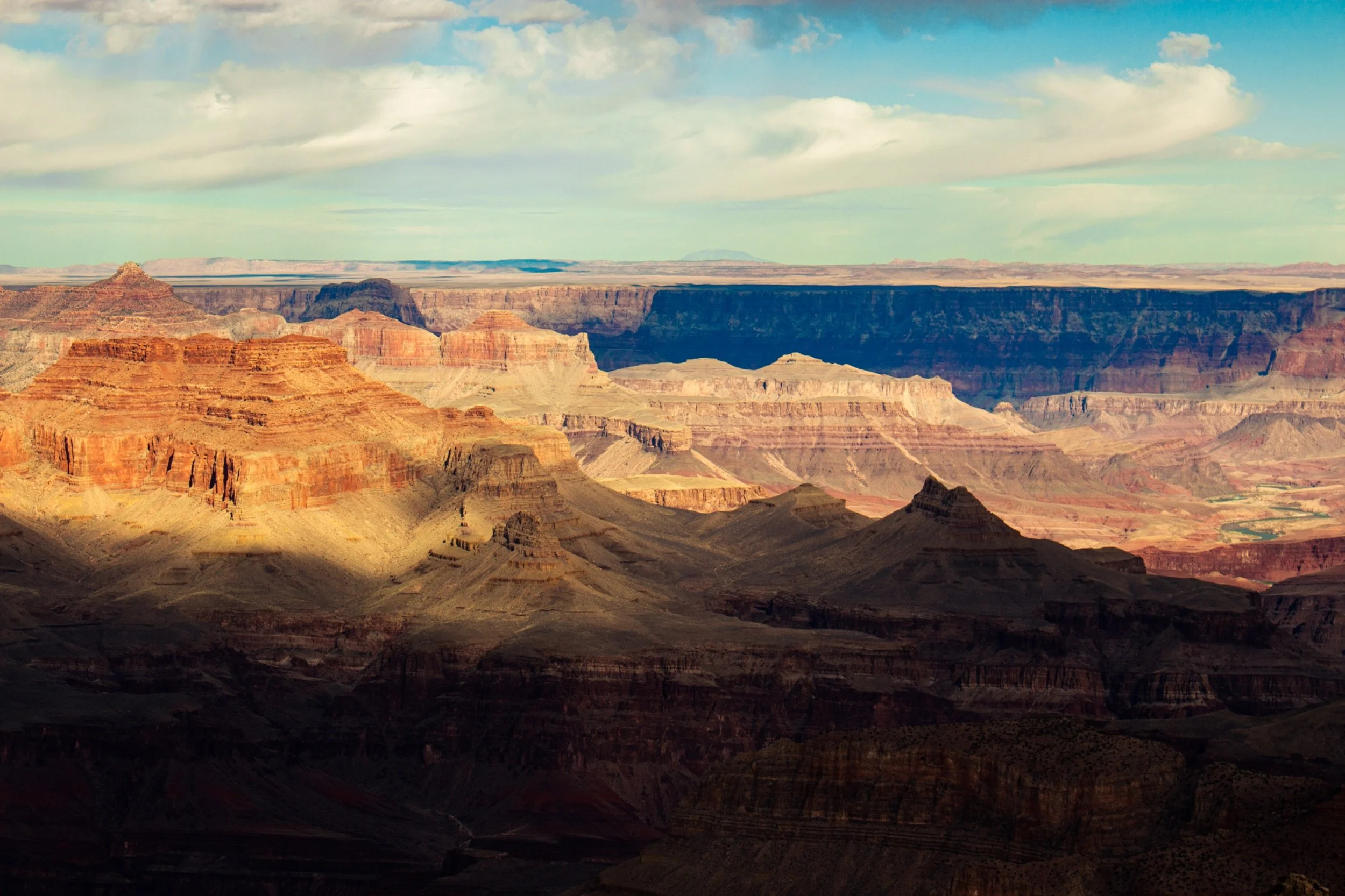 Scenic view of the Grand Canyon with layered rock formations, colorful cliffs, and a partly cloudy sky overhead.