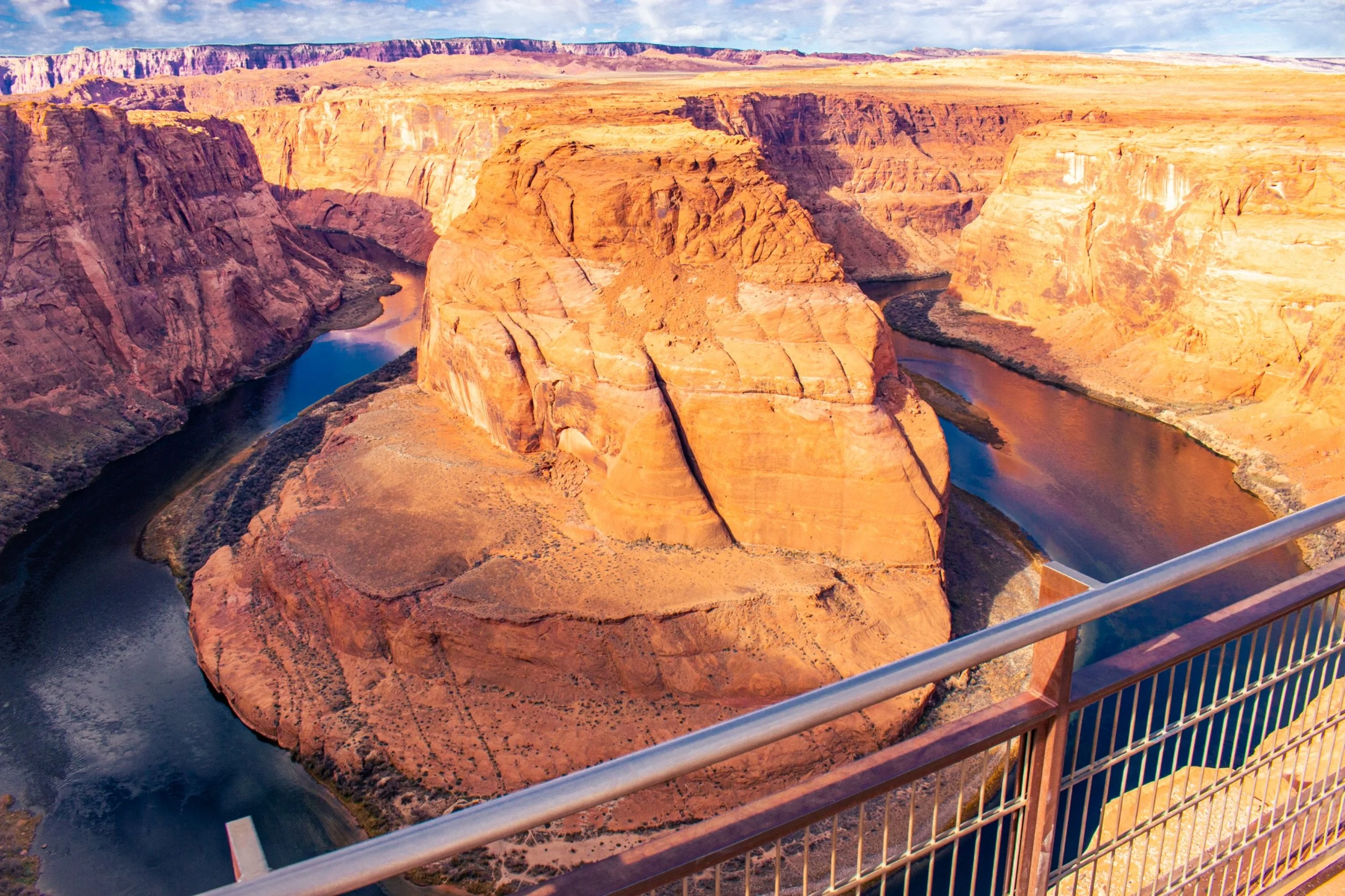 View of the Grand Canyon with Colorado River flowing at the bottom, taken from a viewing platform with a metal railing.