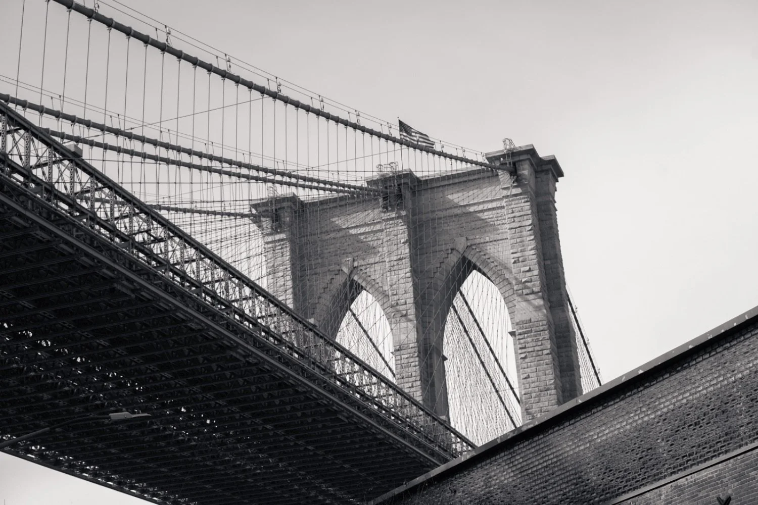 A black-and-white photo of the Brooklyn Bridge in New York City, showing the stone arches and suspension cables.