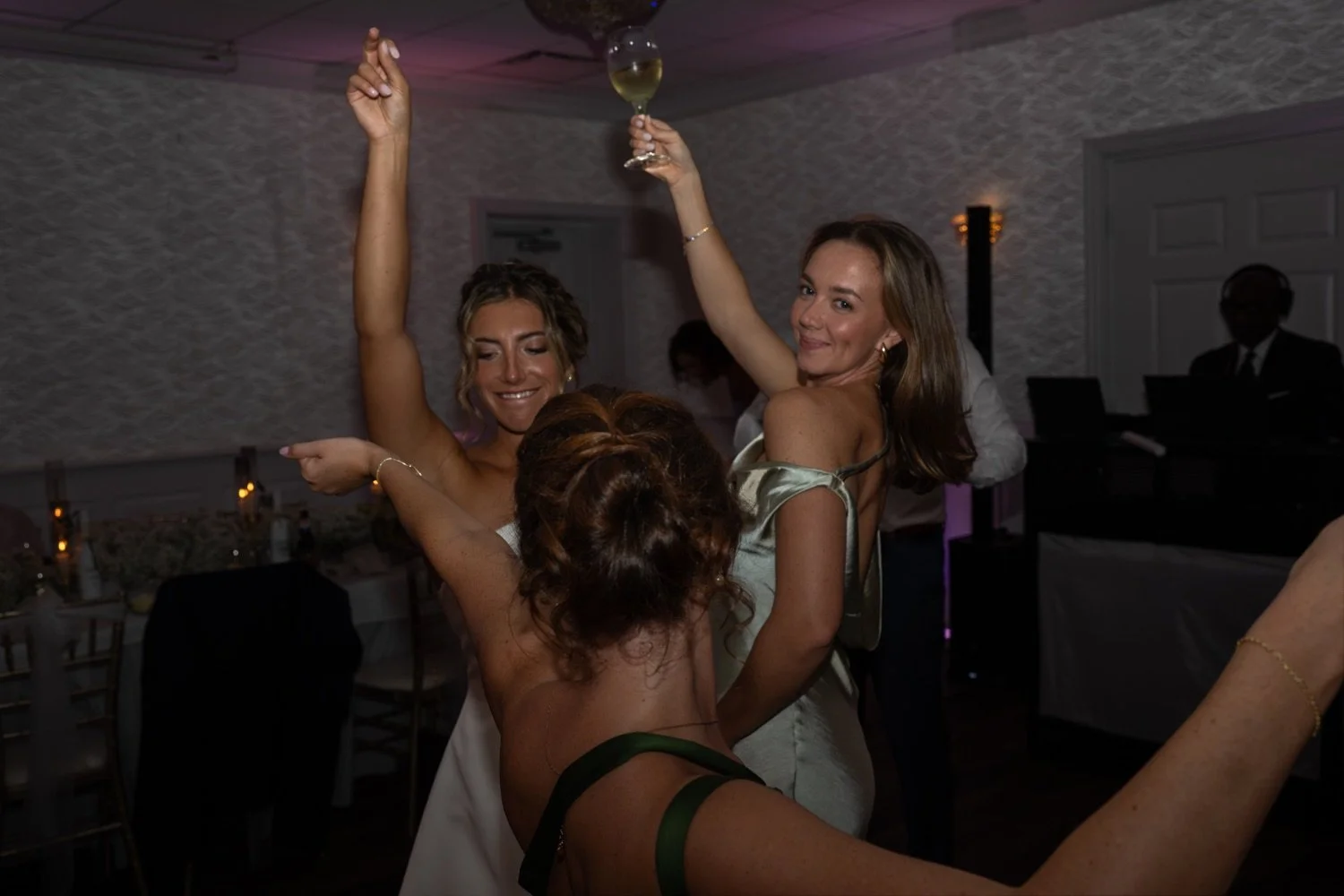 Three women dancing and celebrating at a party, one winking and holding a wine glass.