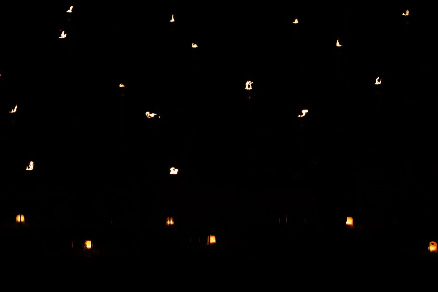 Multiple small candles or lanterns with flames in a dark setting.