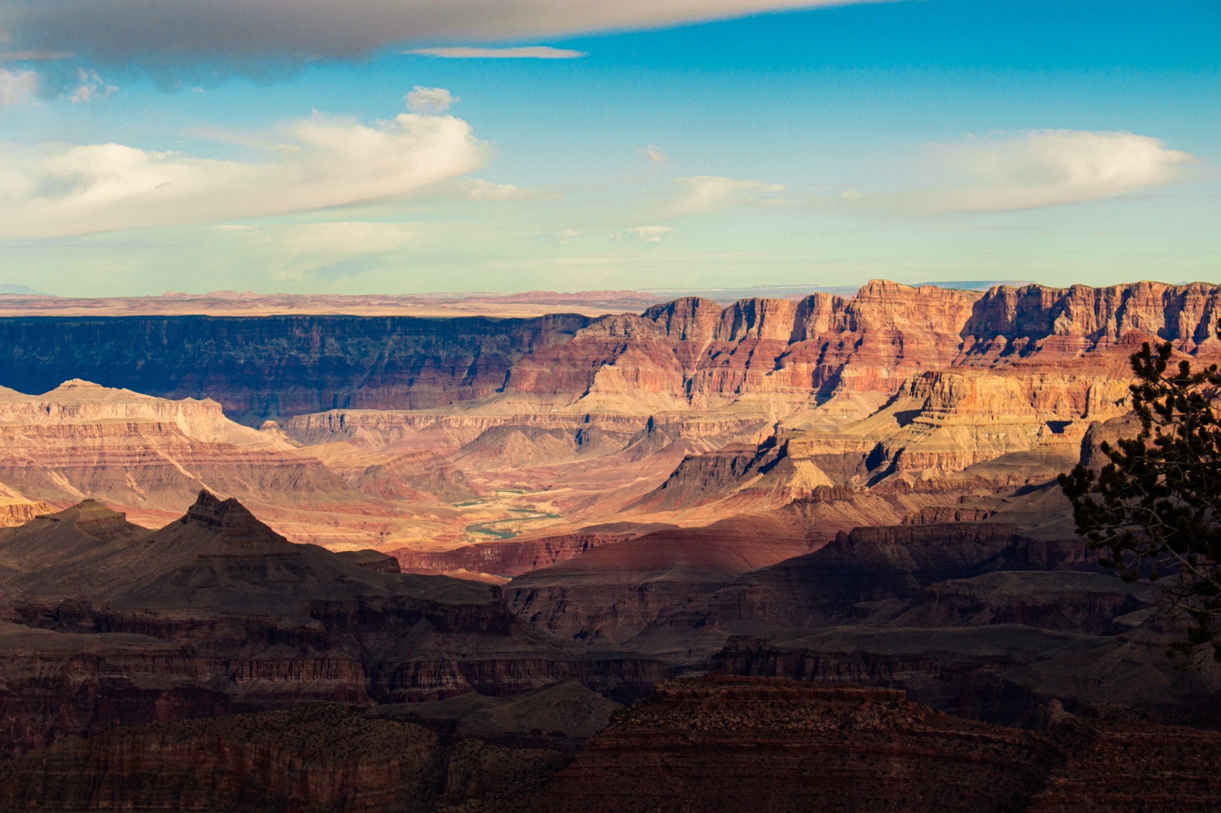 A landscape view of the Grand Canyon featuring layered rock formations in various shades of red, orange, and brown under a partly cloudy sky.
