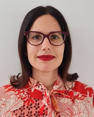 A woman with dark hair, wearing glasses and red lipstick, dressed in a red and white patterned blouse.