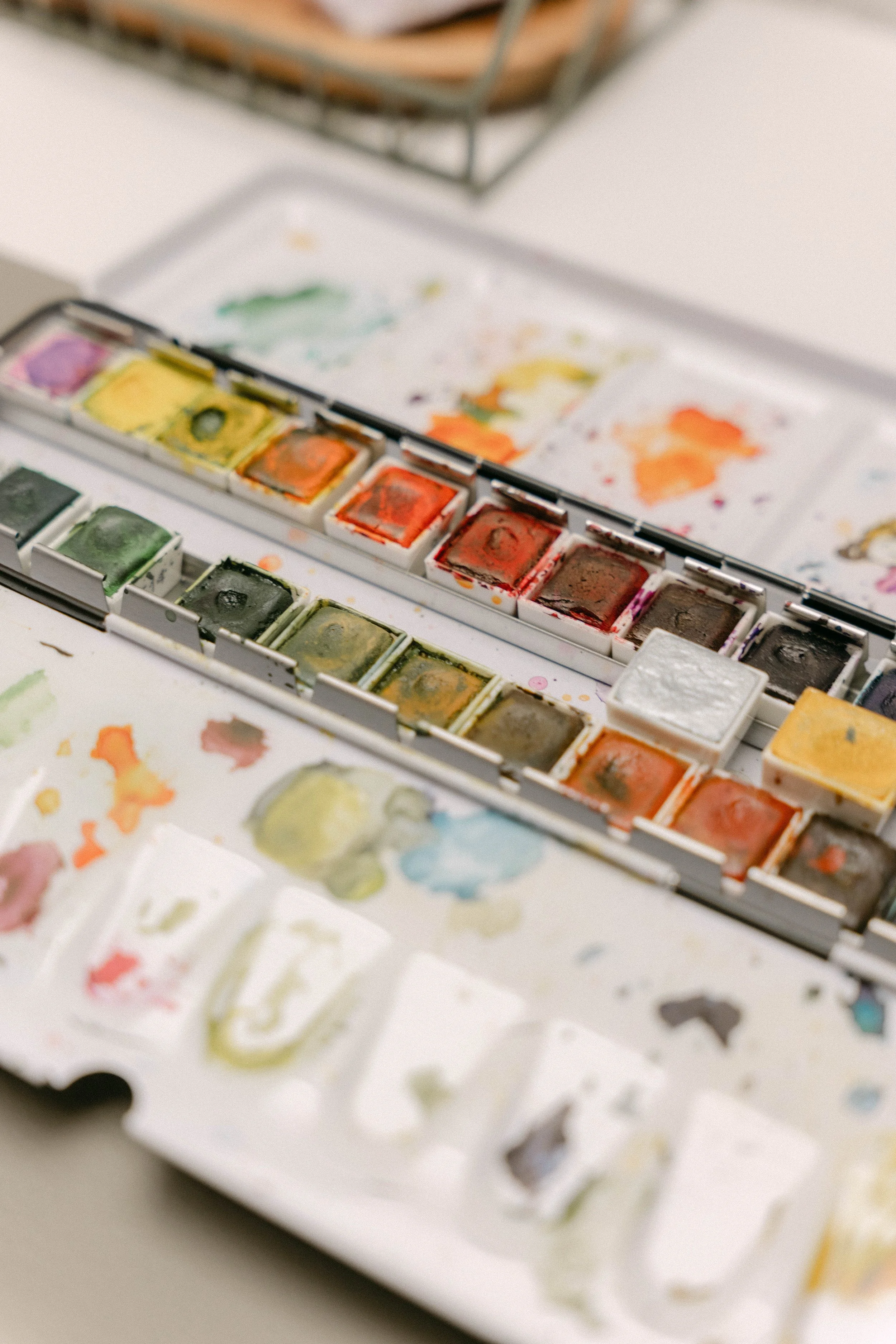 A watercolor paint set with various colors, some mixed on a palette, and watercolor papers with paint swatches and sketches.