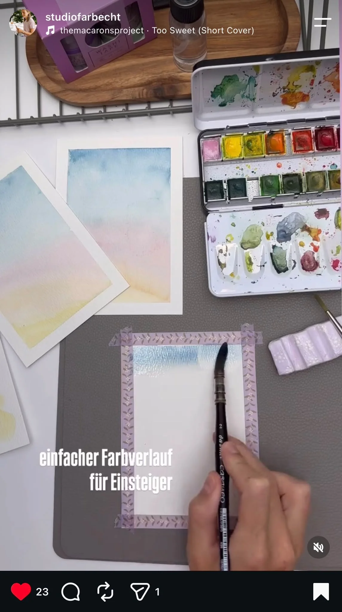 Hand zeichnet einen einfachen Farbverlauf für Anfänger auf einem weißen Papier, das mit einer Rahmenlätzchentechnik verziert ist, während Wasserfarbenpalette und Pinsel sichtbar sind.