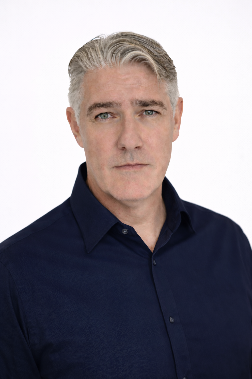 Headshot of a middle-aged man with gray hair and blue eyes, wearing a navy collared shirt, against a plain white background.